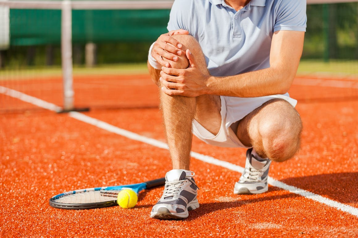 Man holding his knee on a tennis court
